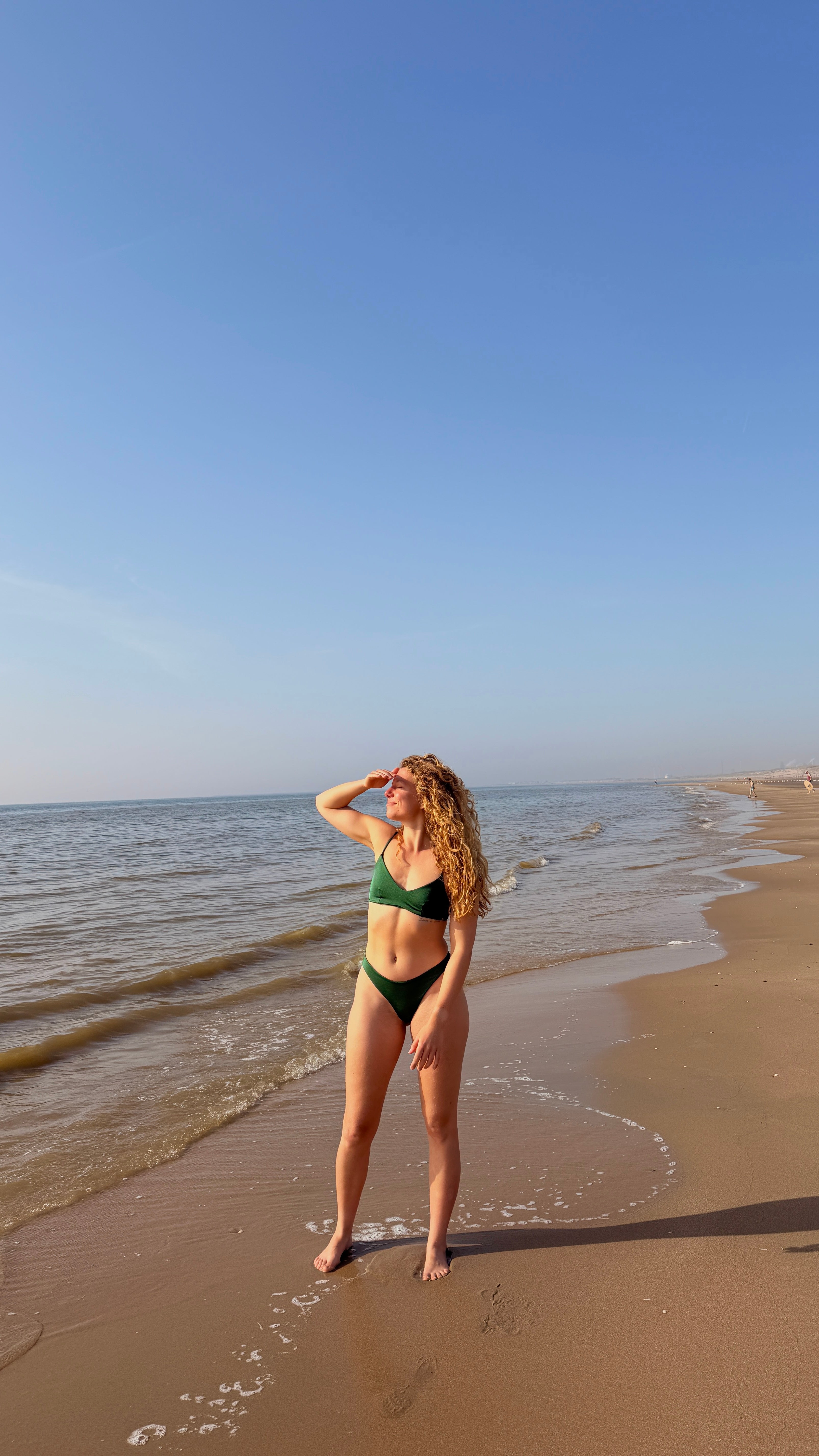 model in groene bralette bikini van pavo couture poserend op strand