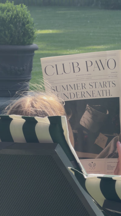 Vrouw op ligbedje in de zon die krant Club Pavo leest